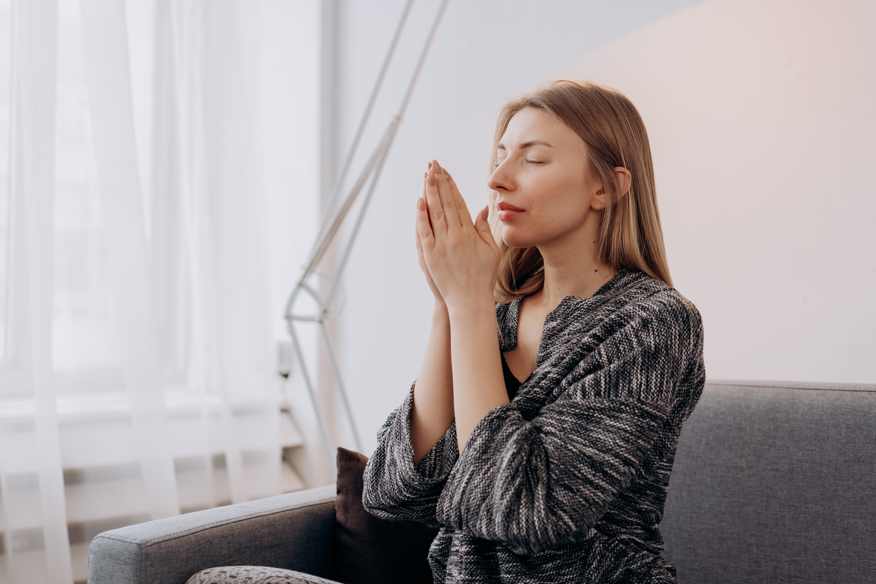 Woman in Black Long Sleeve Shirt Sitting on Gray Couch Praying